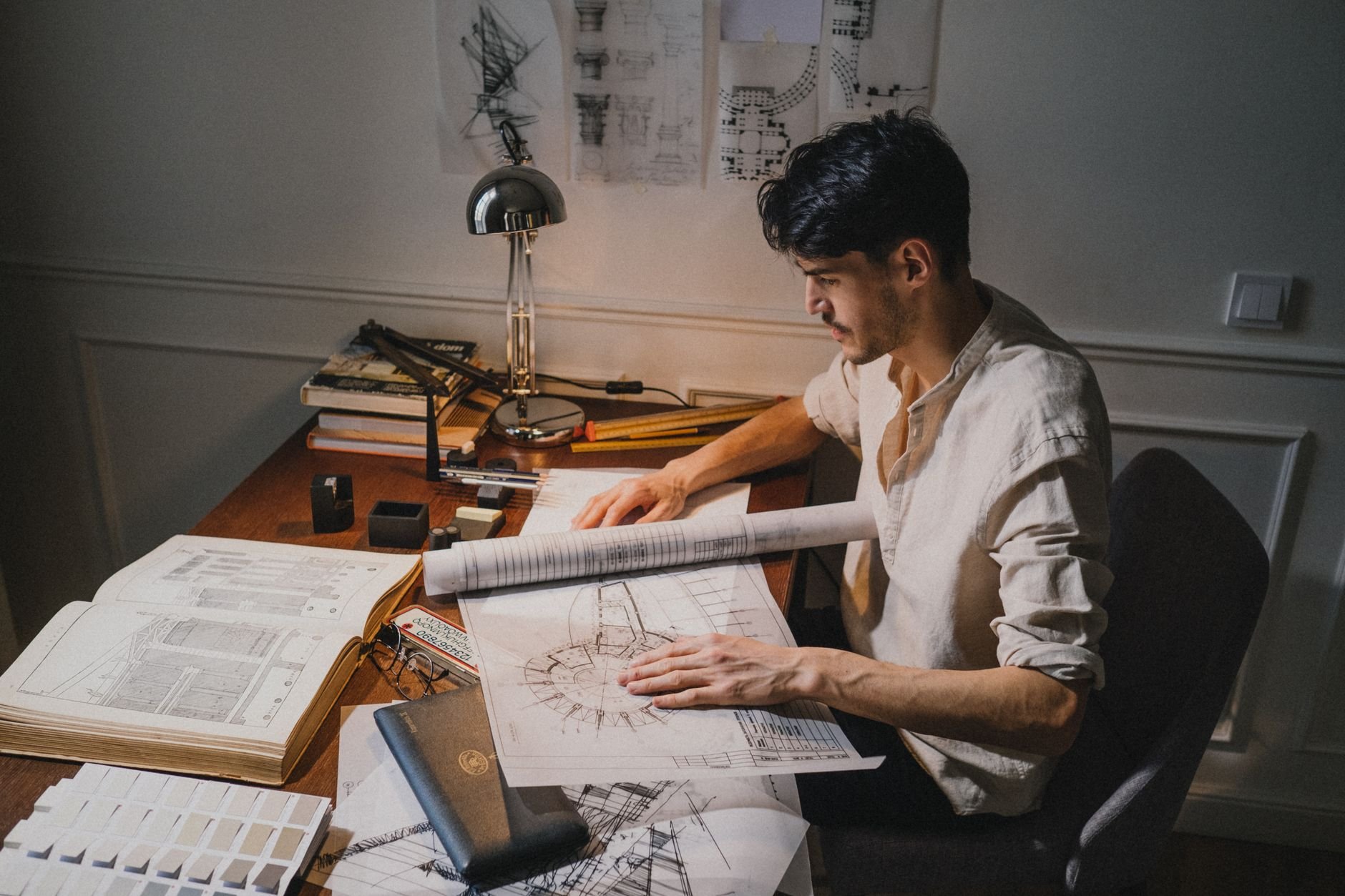 Young architect working on blueprint designs at a studio desk under lamp light